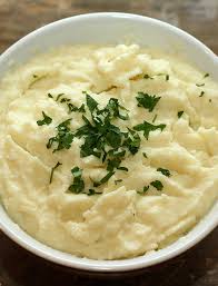 a bowl containing a fluffy white mashed vegetable topped with fresh herbs. 