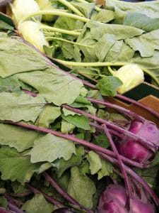 A photo of Kohlrabi in a cardboard box. There are two types shown, green and purple