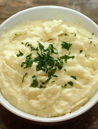 a bowl containing a fluffy white mashed vegetable topped with fresh herbs.